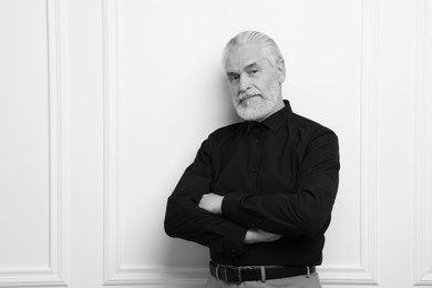 Portrait of handsome senior man against light wall, space for text. Black and white effect