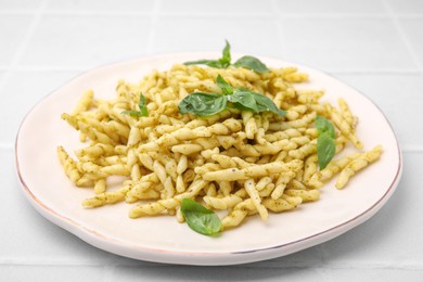 Photo of Plate of delicious trofie pasta with pesto sauce and basil leaves on white tiled table, closeup