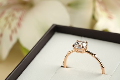 Photo of Beautiful engagement ring in box against blurred background, closeup. Space for text