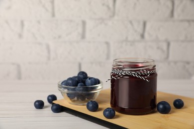 Photo of Jar of delicious blueberry jam and fresh berries on white wooden table, space for text