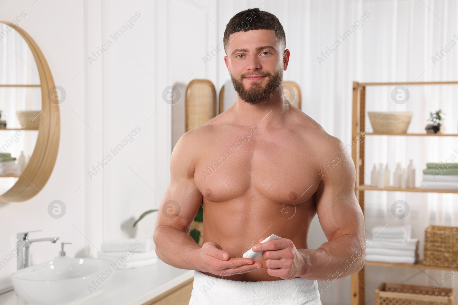 Photo of Handsome man applying body cream in bathroom