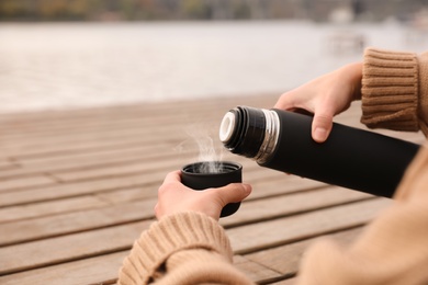 Woman pouring drink from thermos into cap at wooden table outdoors, closeup. Space for text