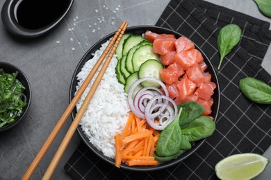 Delicious poke bowl with salmon and vegetables served on grey table, flat lay