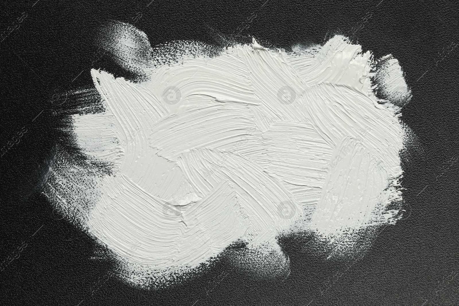 Photo of Strokes of white oil paint on black canvas, top view