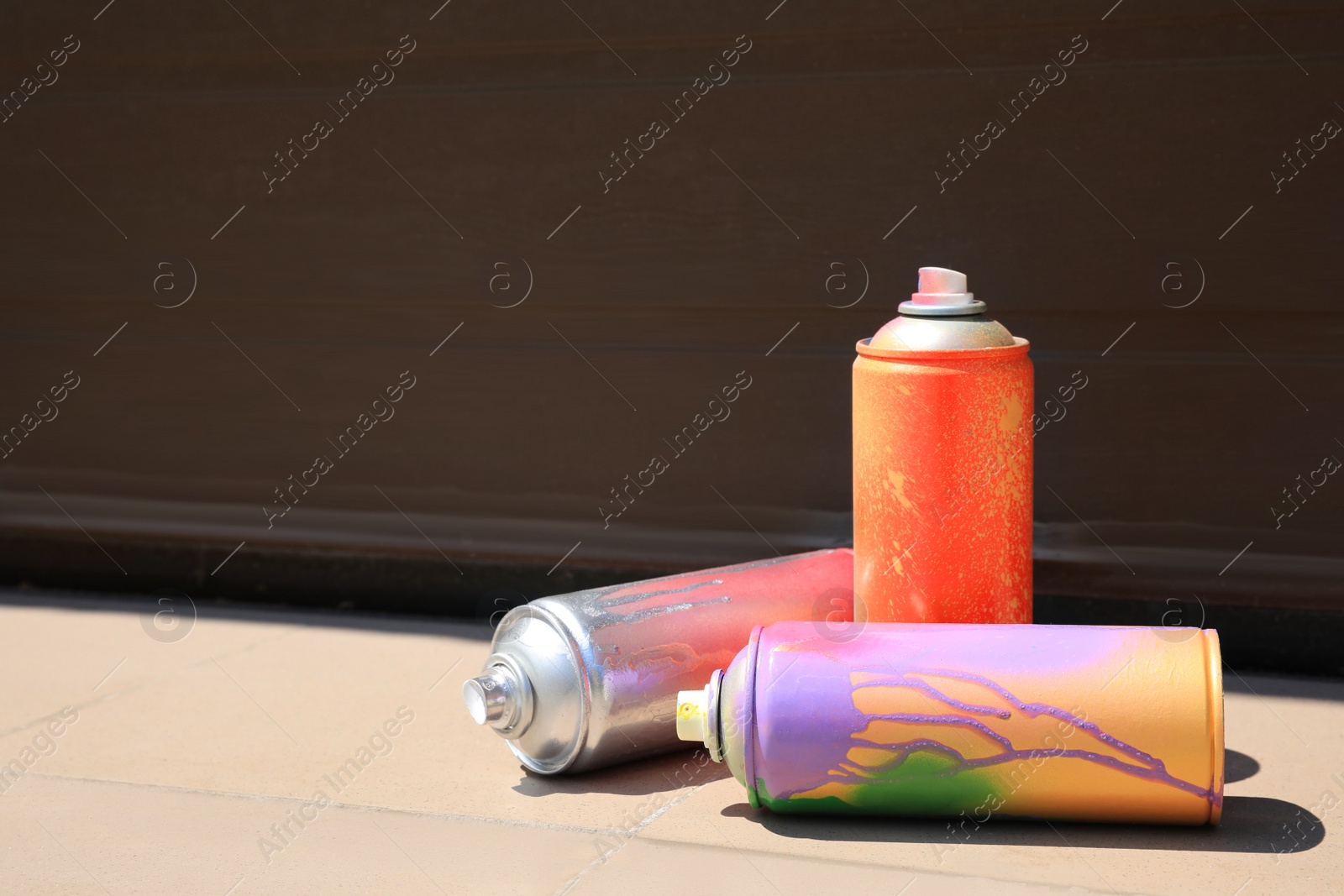 Photo of Used cans of spray paint on tile floor near black wall outdoors, space for text. Graffiti supplies