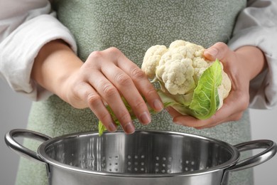 Photo of Woman separating fresh cauliflower cabbage above colander, closeup