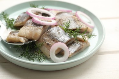 Photo of Plate with sliced salted herring fillet, onion rings and dill on white wooden table, closeup