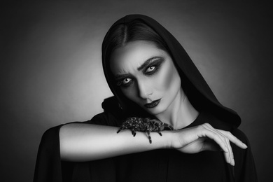 Photo of Mysterious witch with spooky spider on dark background. Black and white effect