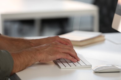 Photo of Man using modern computer keyboard at white desk in office, closeup