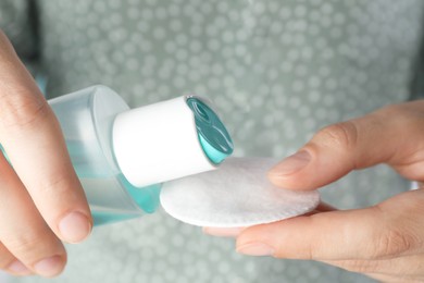 Photo of Woman pouring micellar water from bottle on cotton pad, closeup