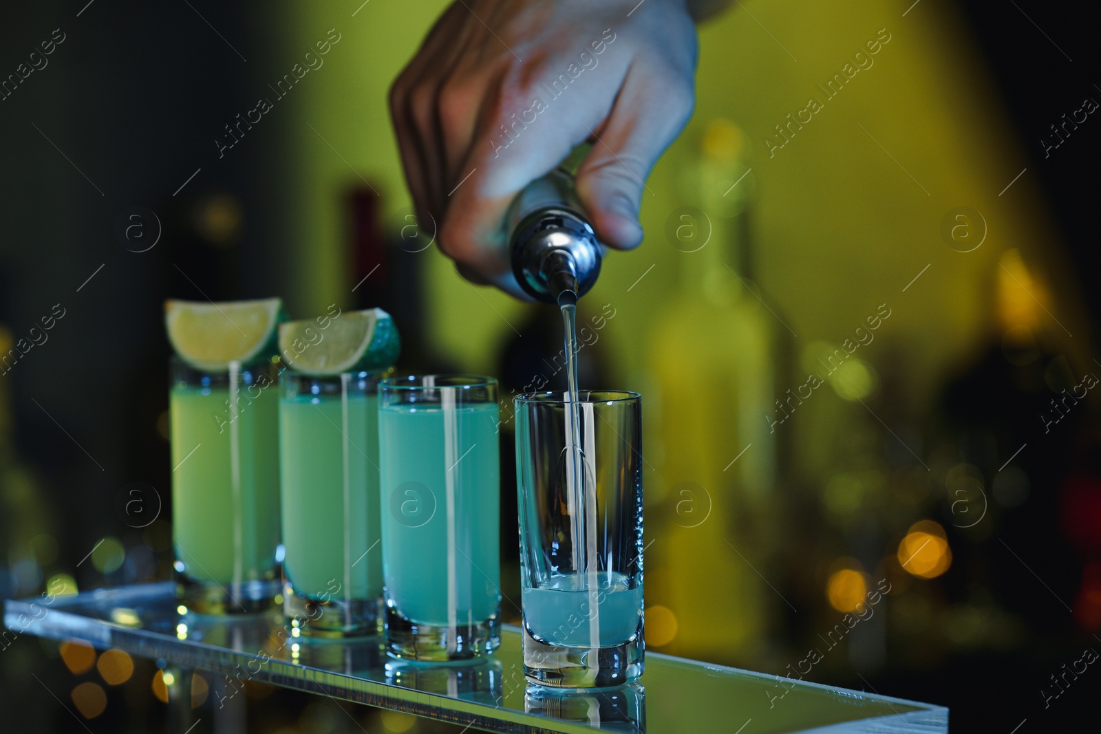 Photo of Bartender pouring alcohol drink into shot glass on blurred background, closeup. Space for text