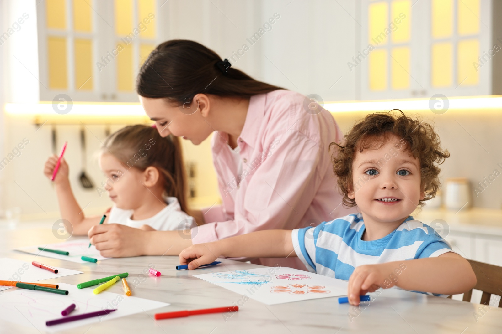 Photo of Mother and her little children drawing with colorful markers at table in kitchen