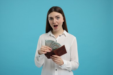 Woman putting money into wallet on light blue background