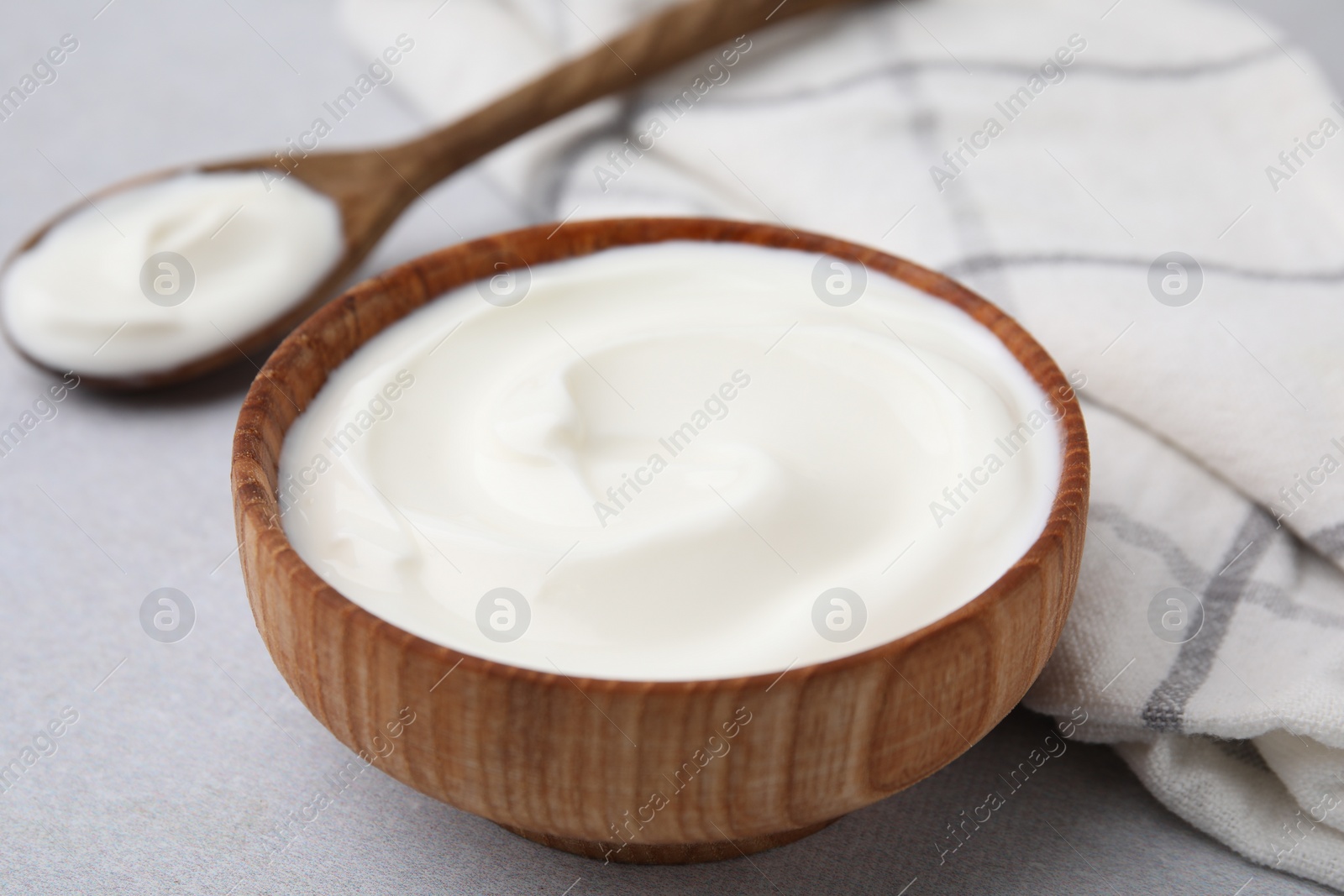 Photo of Delicious natural yogurt in bowl and spoon on light grey table, closeup