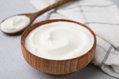 Delicious natural yogurt in bowl and spoon on light grey table, closeup