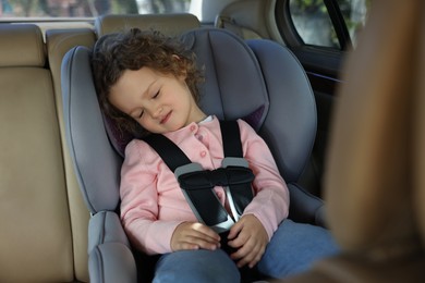 Photo of Cute little girl sleeping in child safety seat inside car