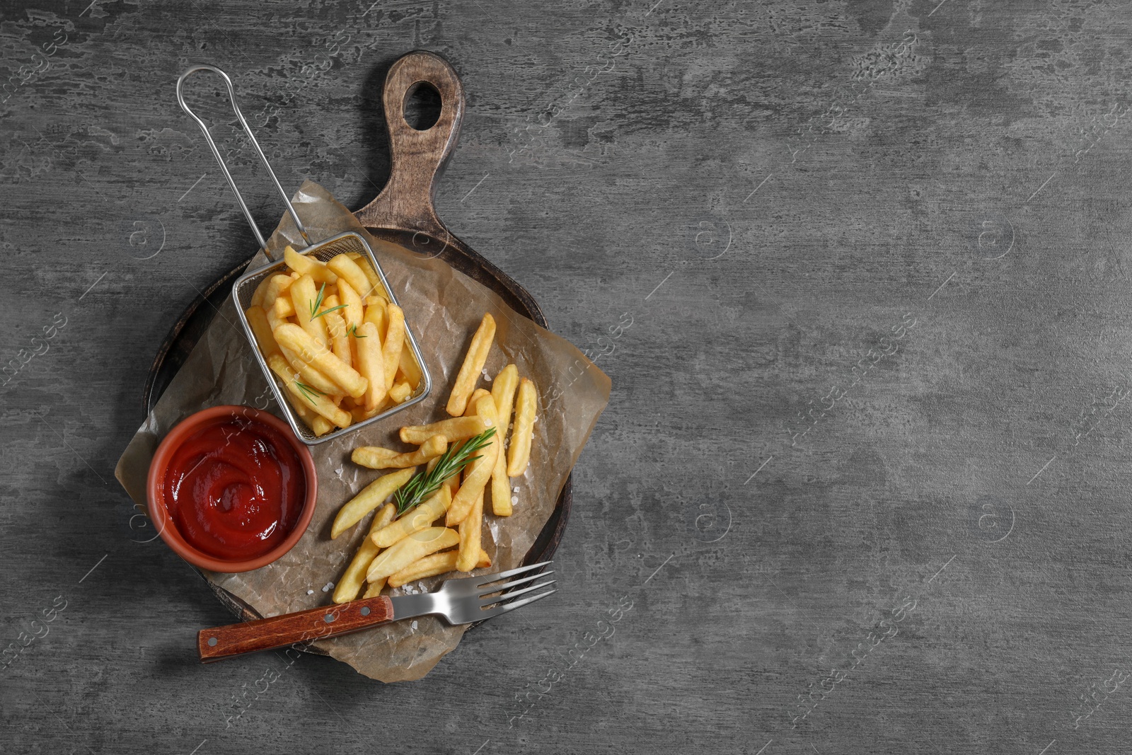 Photo of Tasty French fries, ketchup and rosemary on grey table, top view. Space for text