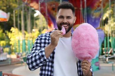 Photo of Happy young man eating cotton candy at funfair