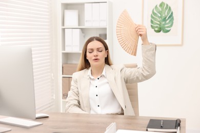 Photo of Businesswoman waving hand fan to cool herself at table in office