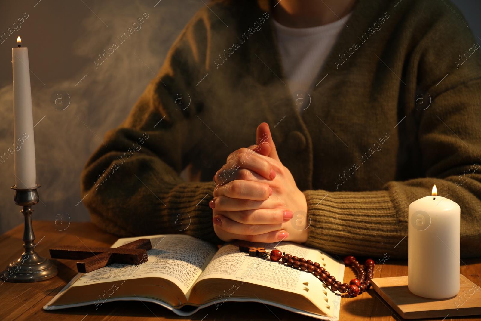 Photo of Woman praying at table with burning candles and Bible, closeup