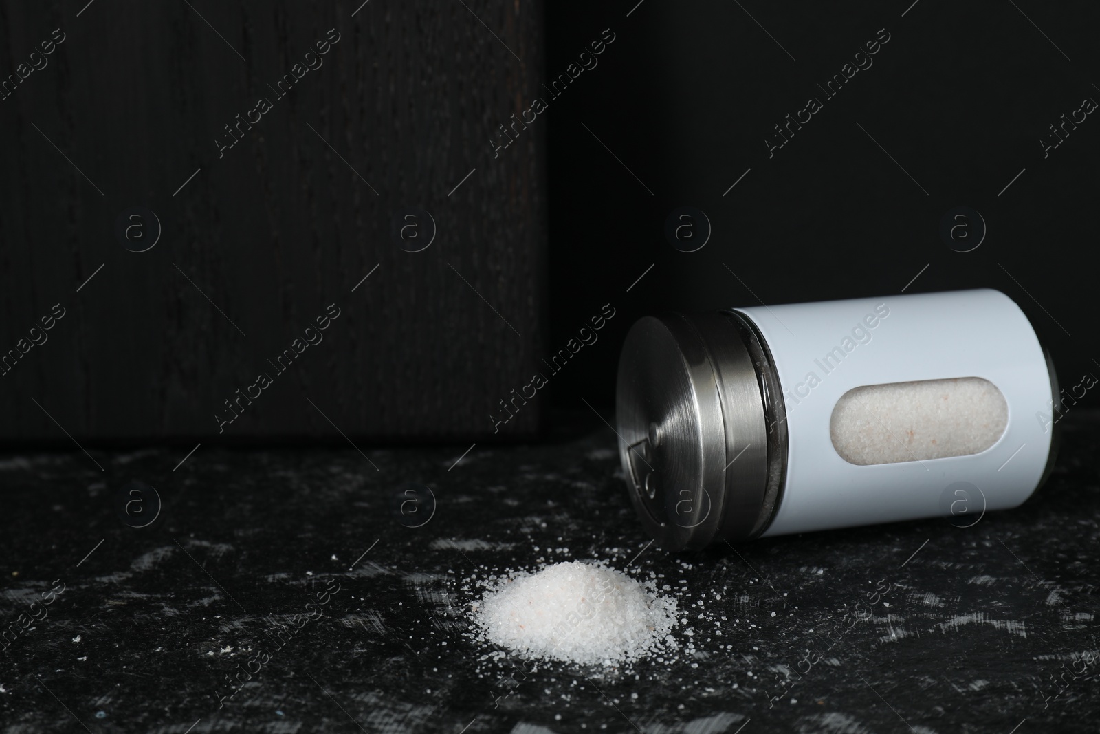 Photo of Overturned shaker with salt on dark table. Space for text