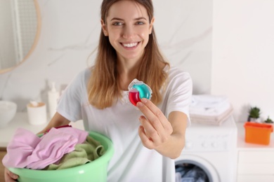 Woman holding dirty clothes and laundry detergent capsule in bathroom, focus on hand