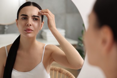 Photo of Woman with dry skin looking at mirror in bathroom