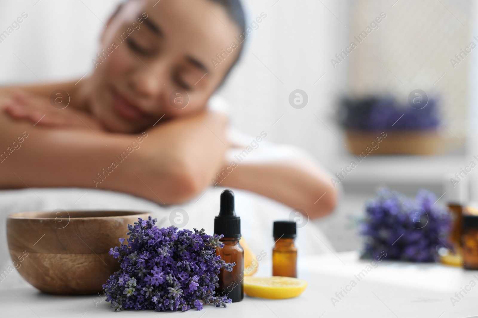 Photo of Woman relaxing on massage couch and bottles of essential oil with ingredients on table in spa salon, selective focus