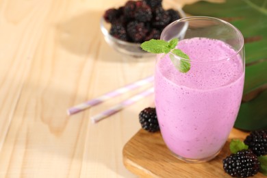 Photo of Delicious blackberry smoothie in glass and berries on wooden table, space for text