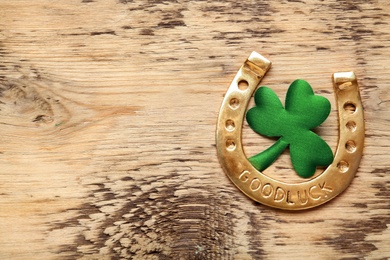 Photo of Golden horseshoe and decorative clover leaf on wooden table, flat lay with space for text. Saint Patrick's Day celebration