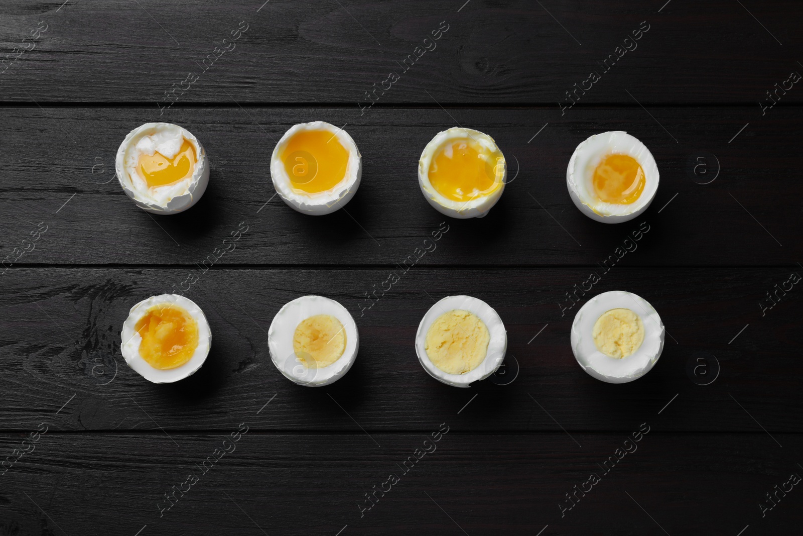 Photo of Different readiness stages of boiled chicken eggs on black wooden table, flat lay