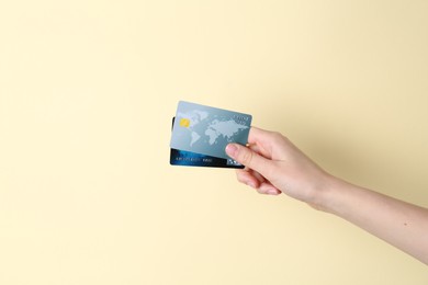 Woman holding credit cards on pale yellow background, closeup