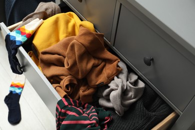 Photo of Cluttered chest of drawers indoors. Clothes in mess