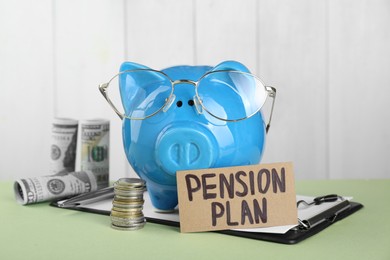 Photo of Card with phrase Pension Plan, piggy bank and money on light green table. Retirement concept