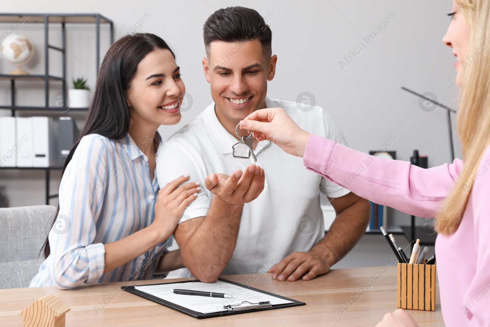 Photo of Real estate agent giving house key to couple at table in office
