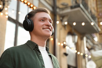 Photo of Smiling man in headphones listening to music outdoors. Space for text