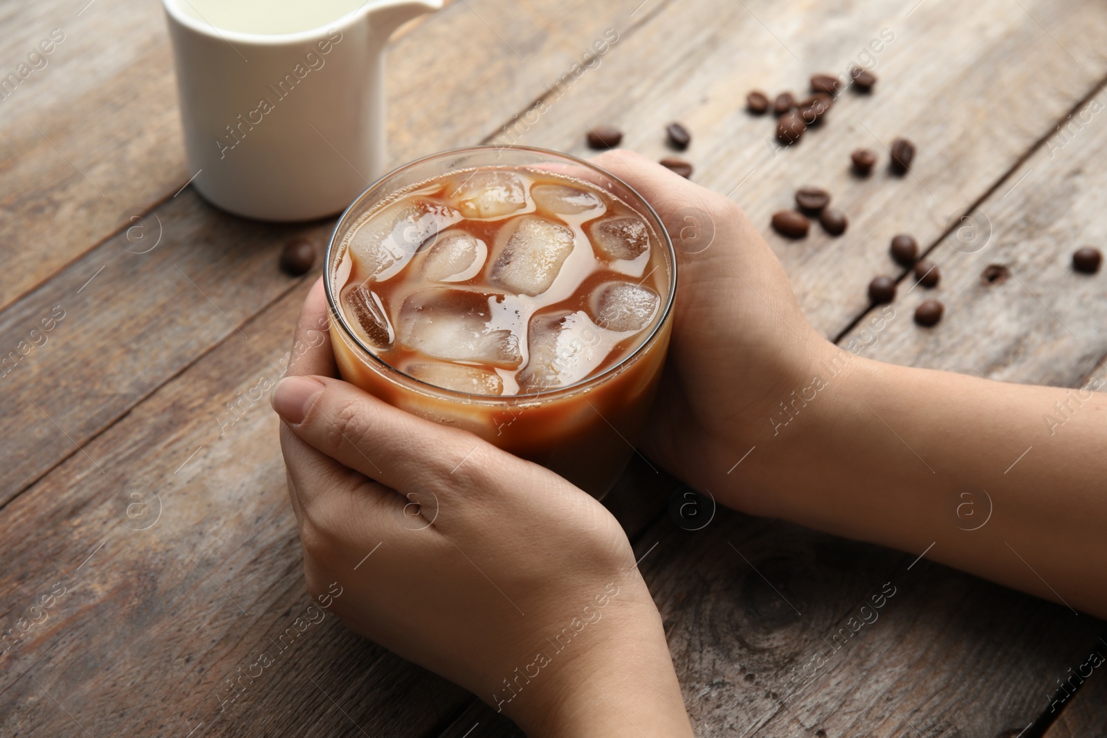 Photo of Woman holding glass of coffee with ice cubes at table, closeup