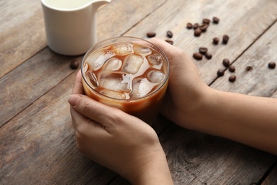 Woman holding glass of coffee with ice cubes at table, closeup