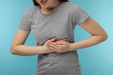 Photo of Woman suffering from stomach pain on light blue background, closeup