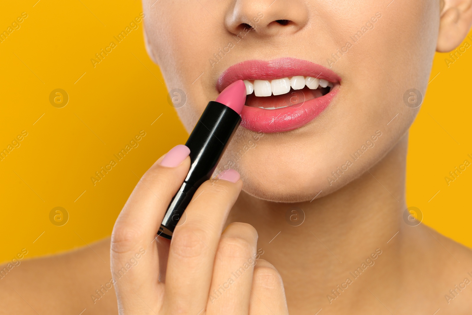 Photo of Young woman applying lipstick on color background, closeup