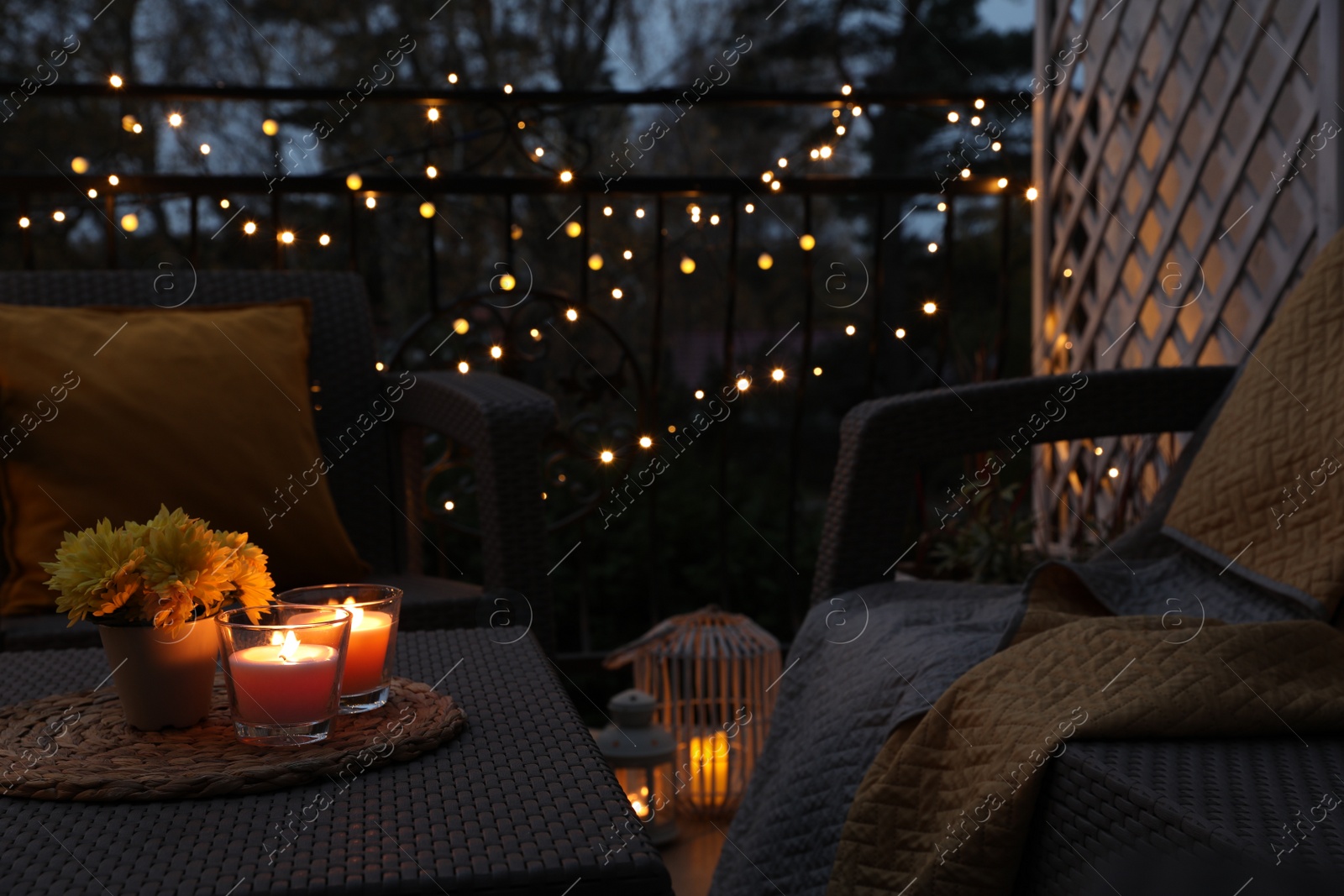 Photo of Beautiful view of garden furniture with pillow, soft blanket and burning candles at balcony