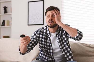 Photo of Emotional man with remote controller watching TV at home