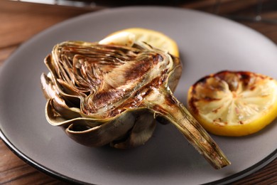 Tasty grilled artichoke and slices of lemon on table, closeup