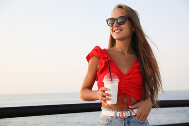 Photo of Beautiful woman with tasty milk shake near sea, space for text
