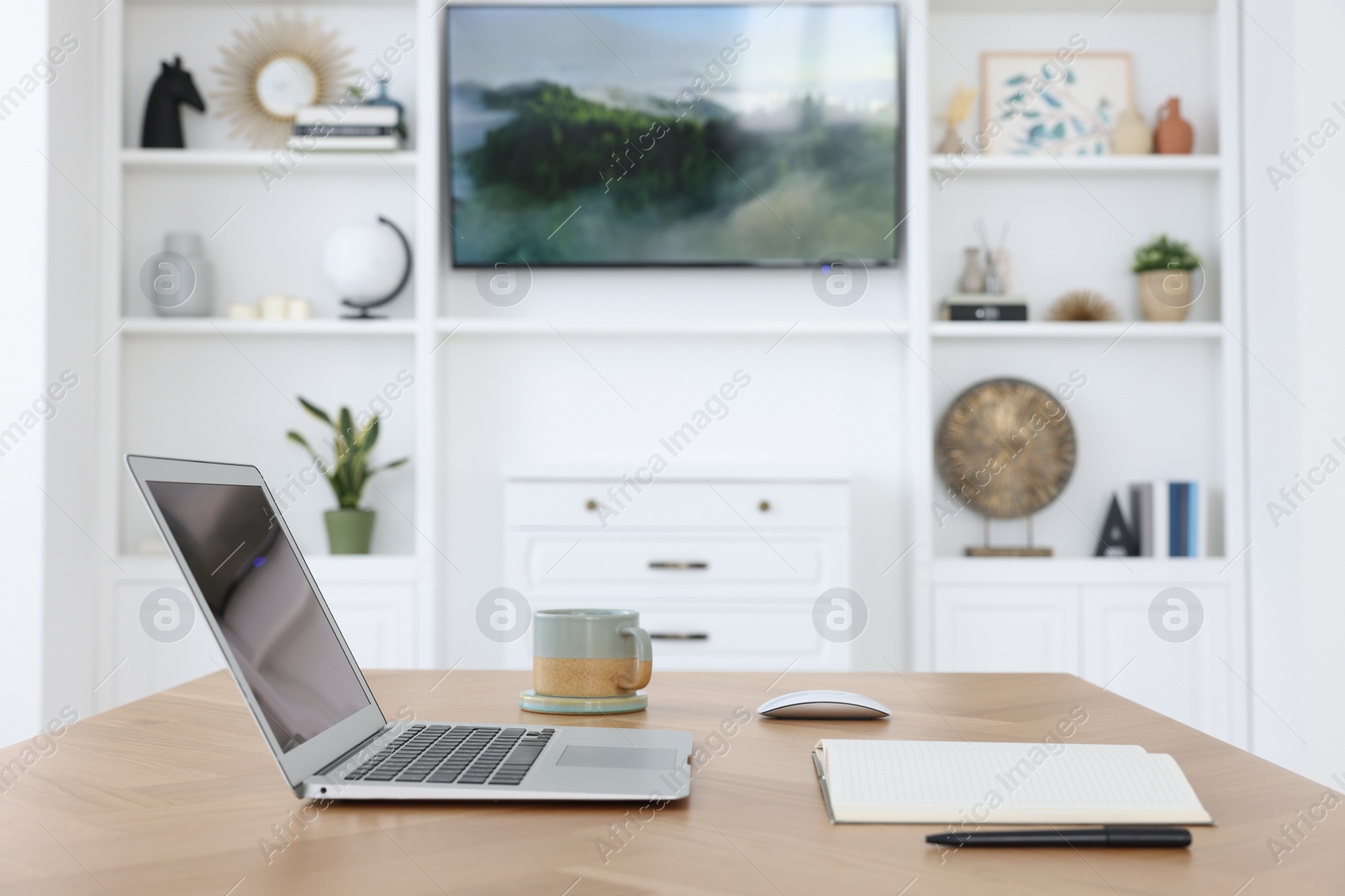 Photo of Interior design. Cosy workplace with laptop on wooden table near tv area