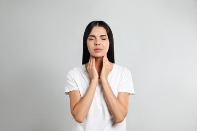 Young woman doing thyroid self examination on light background