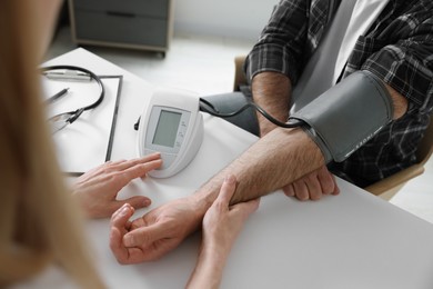 Photo of Doctor measuring blood pressure of man at table indoors, closeup