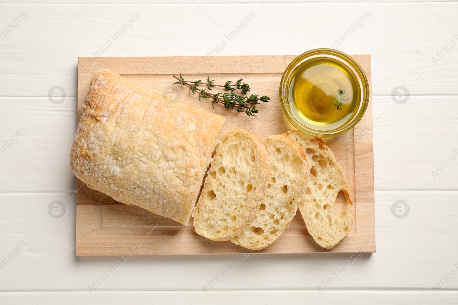 Photo of Bowl of olive oil, thyme and bread on white wooden table, flat lay