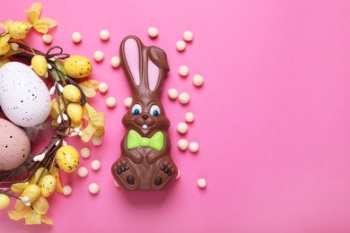 Flat lay composition with chocolate Easter bunny, festively decorated eggs and candies on pink background. Space for text