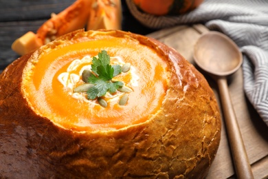 Tasty pumpkin cream soup served in bread on table, closeup